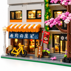 Sushi storefront close-up with orange awning, cherry blossoms, and warm LED-lit interior