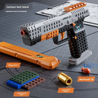 A toy block pistol set shown on a gray grommet mat with included parts and labels: orange magazine, green and blue building block bag, gold eggshell pieces, red warheads, and a black/gray/orange assembled pistol. Text reads 'Cartoon tech black' and 'CONTINUOUS BURST OF PLEASURE.