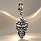 The silver skull pendant keychain linked to automotive remote fobs and house keys on a rustic wooden table.