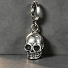 The silver skull keychain attached to a set of automotive keys and a remote fob resting on a dark wood table.
