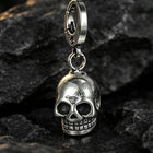 An adult palm holding the solid silver skull key fob to display its handheld scale, proportion, and reflective sheen.