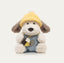 Stuffed toy dog wearing a yellow hat and blue outfit on a beige background