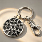 The silver skull compass keychain attached to car keys and a remote fob resting on a rustic wooden surface.