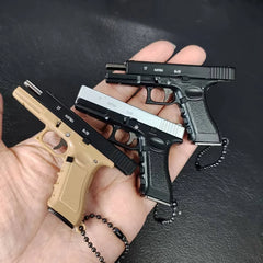 Three mini scale pistol model keychains in multiple colors held in hand, decorative collectibles