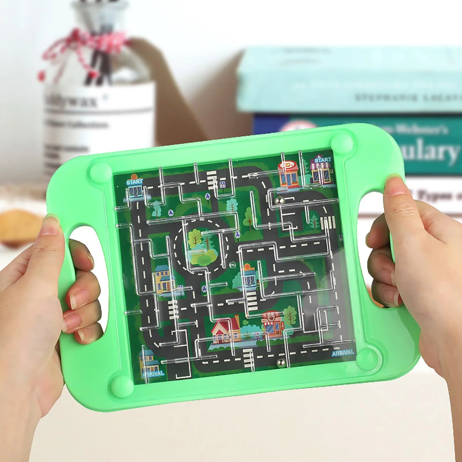 Green toy tablet with a maze design held by hands against a blurred indoor background Main image