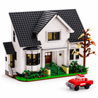 White clapboard Bella House building-block manor with dark roof, green landscaping and red pickup truck, front three-quarter view.