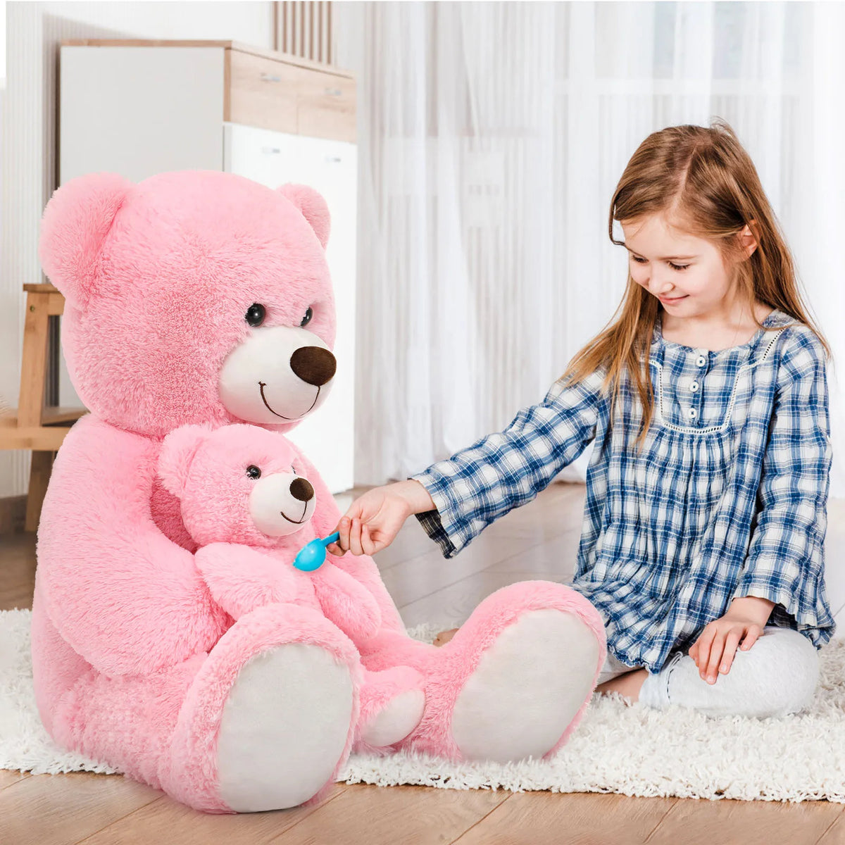 Child playing with a large pink teddy bear in a bright room.