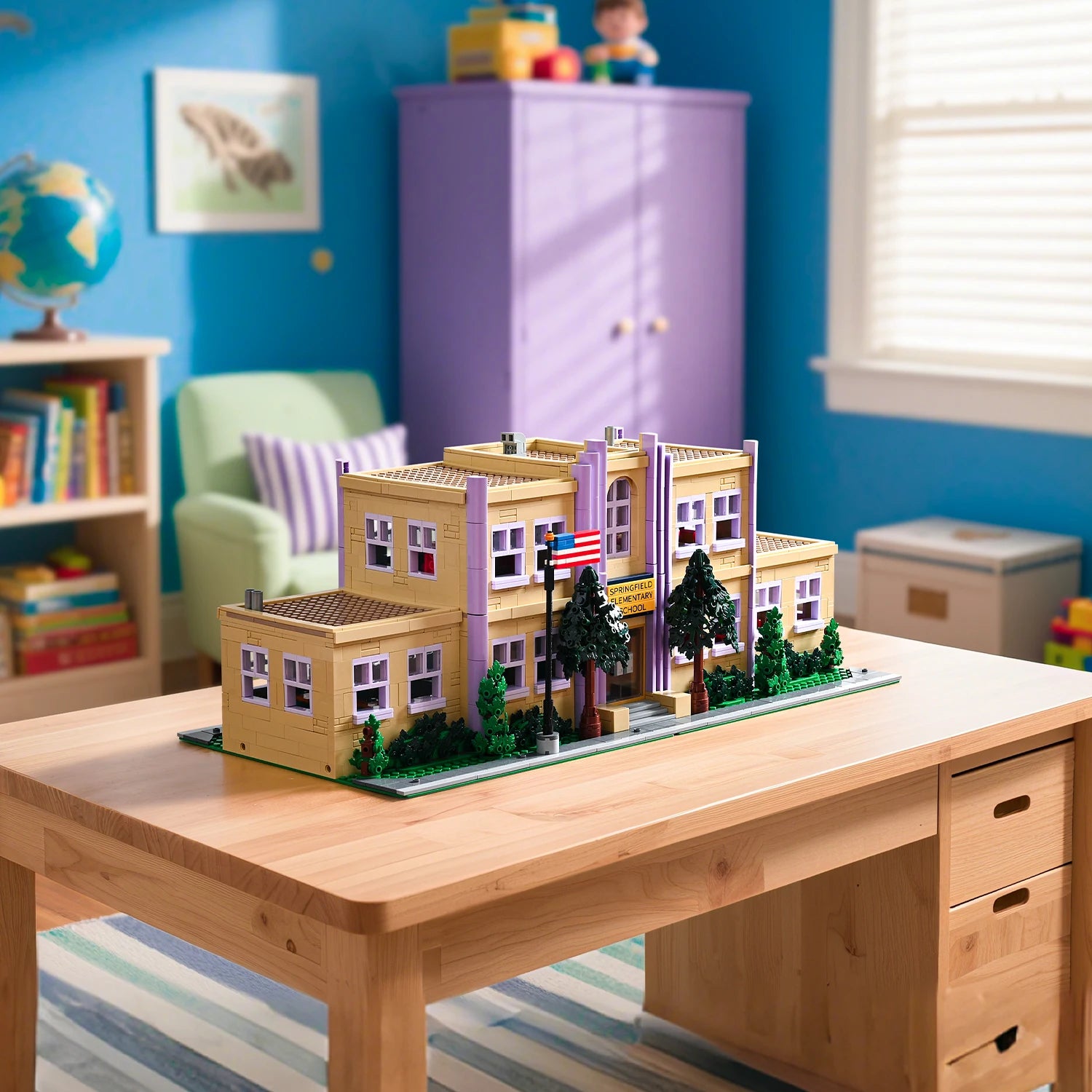 Model of a school building on a wooden desk in a child's room with blue walls and toys.