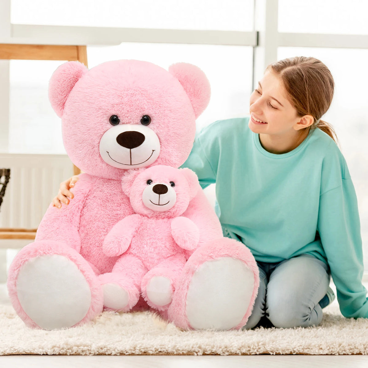 Woman holding two large pink teddy bears in a bright room.