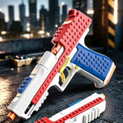 A toy gun-shaped building block set with a red slide, blue grip, white body, and orange tip, shown with a matching magazine on a dark textured surface with a blurred city skyline background.
