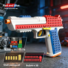 A toy building-block style toy gun in red, blue, and white with orange and yellow accents, shown on a dark blurred background with text overlays reading 'Red and blue' and product details for building blocks, shells, and bullets.