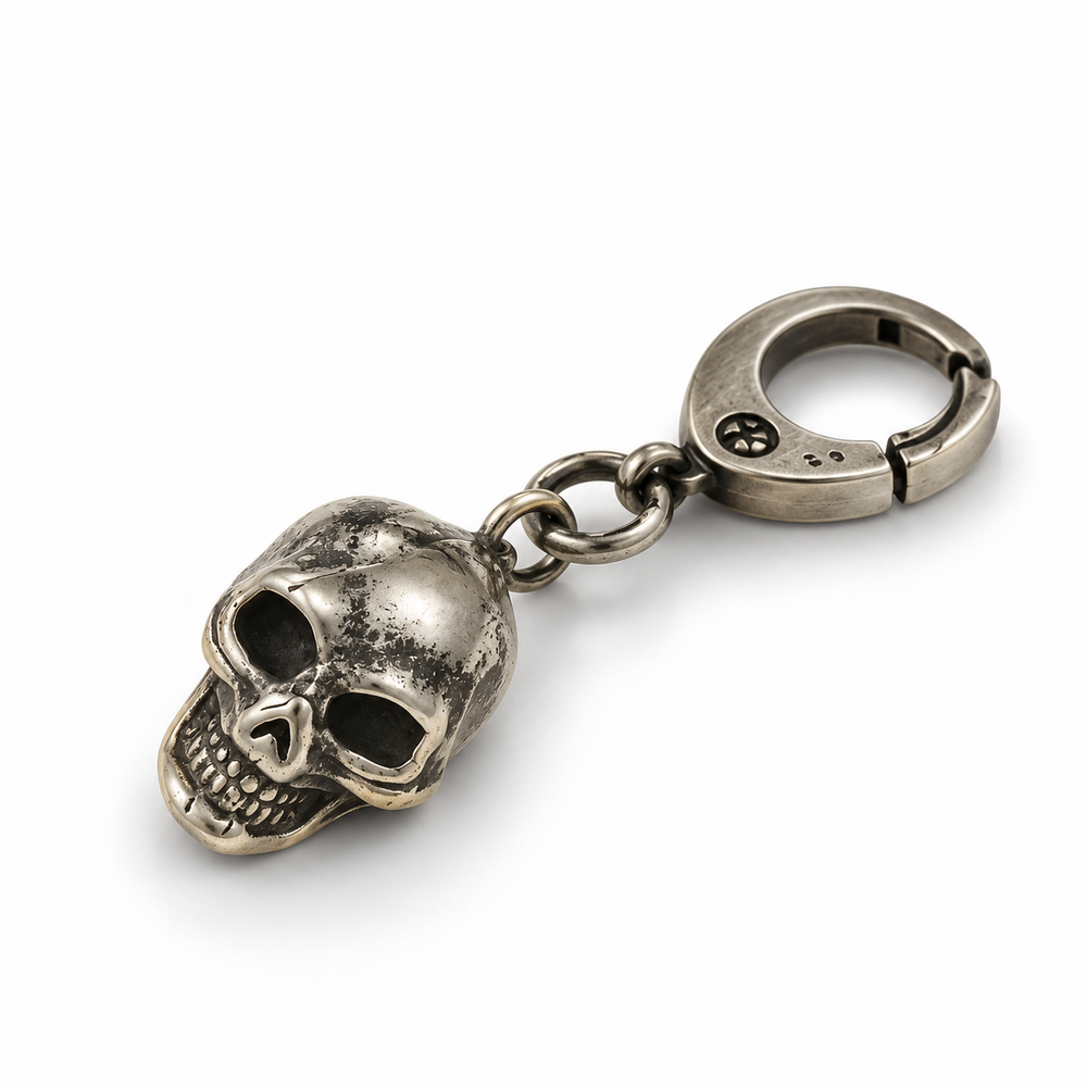 Dark punk antique silver skull keychain with spring clasp, lying on white surface