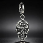 The silver skull pendant keychain hanging along the seam of a front denim jeans pocket.