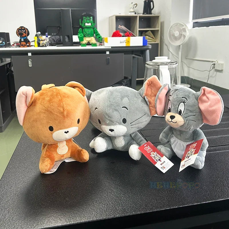 Three plush toys resembling a bear, cat, and mouse on a desk with office items in the background.