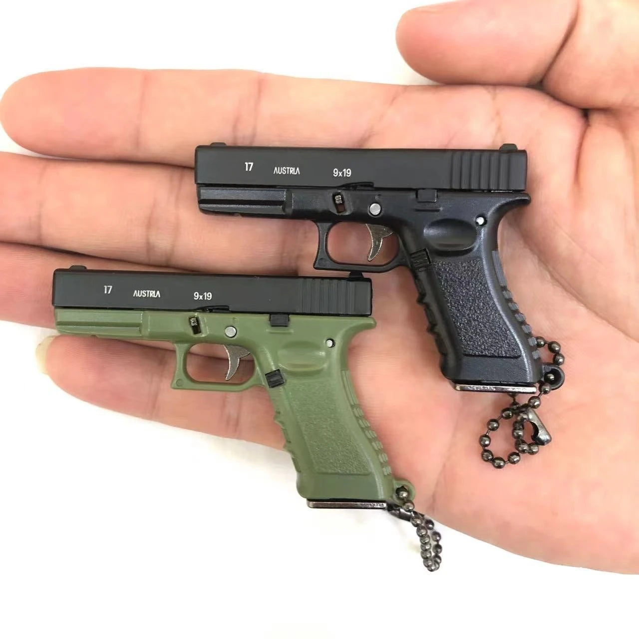 Two mini scale pistol model keychains in black and green held in hand, decorative collectible Main image