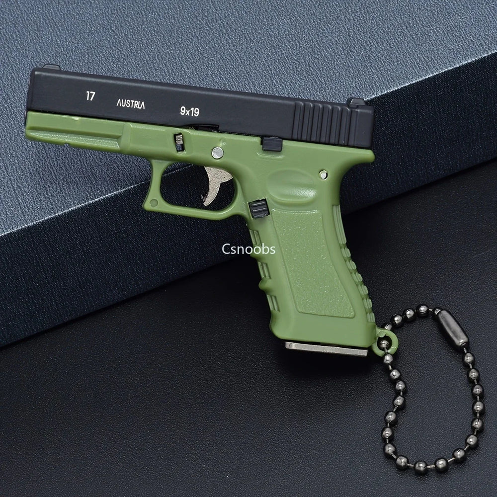 Green and black mini scale pistol model keychain on display box, decorative metal collectible