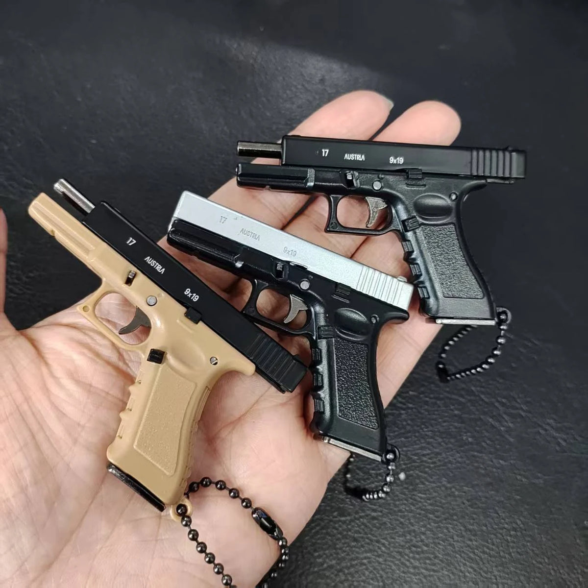 Three mini scale pistol model keychains in multiple colors held in hand, decorative collectibles