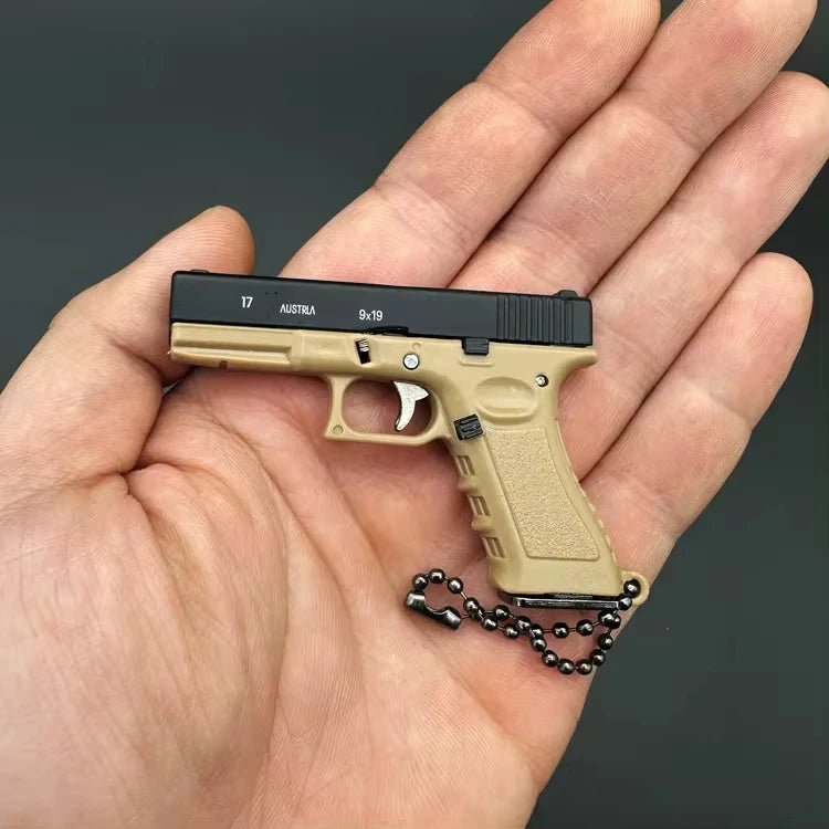 Tan mini scale pistol model keychain held in hand, decorative collectible keychain