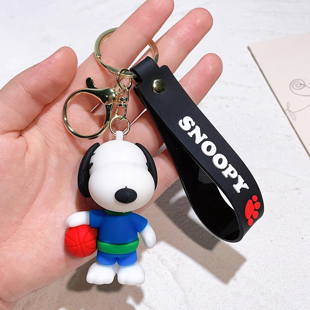 Snoopy keychain with black ‘Snoopy’ strap, held in a hand, featuring Snoopy in a blue outfit holding a red basketball on a white background