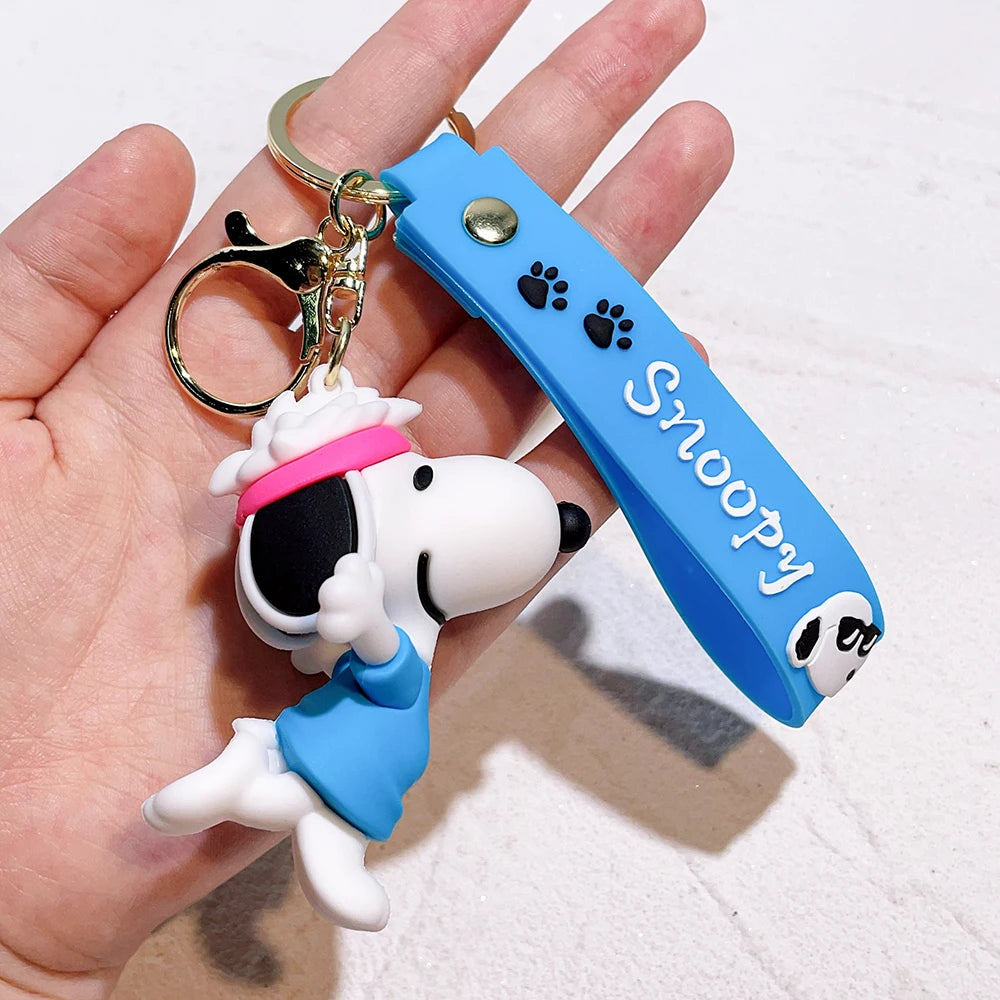 Snoopy silicone keychain wearing blue outfit with pink headband and blue strap held in a hand on a light background