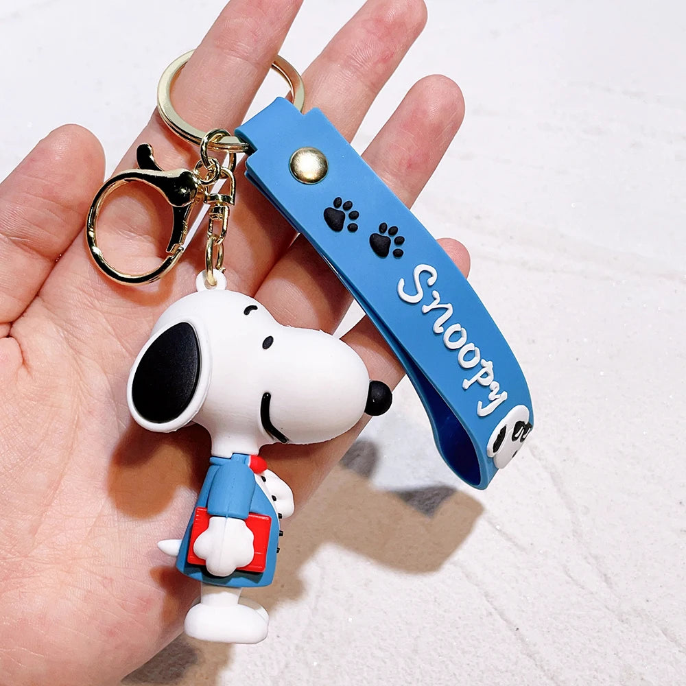 Snoopy silicone keychain with blue strap and book accessory held in a hand on a light background