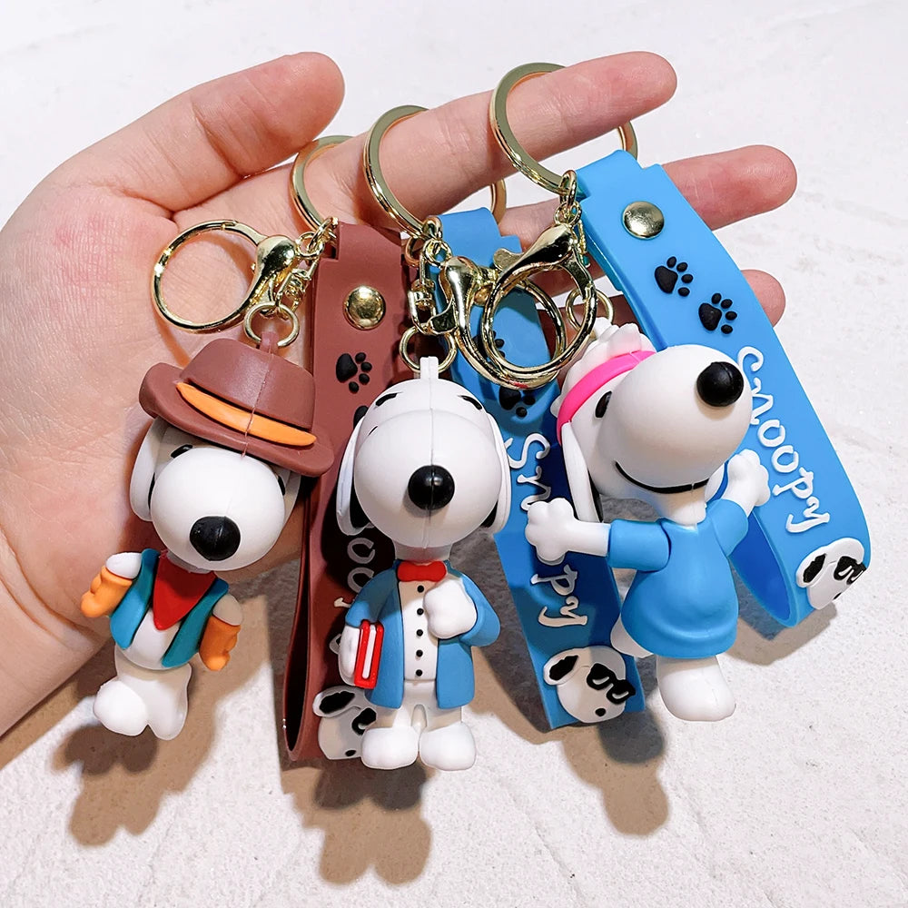 Hand holding a mixed set of Snoopy silicone keychains in different outfits on a white background