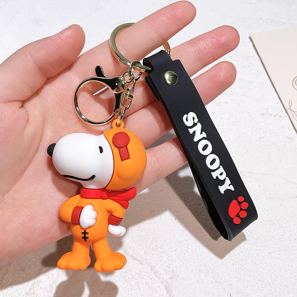Snoopy silicone keychain in orange suit with black ‘SNOOPY’ strap held in a hand on a light background
